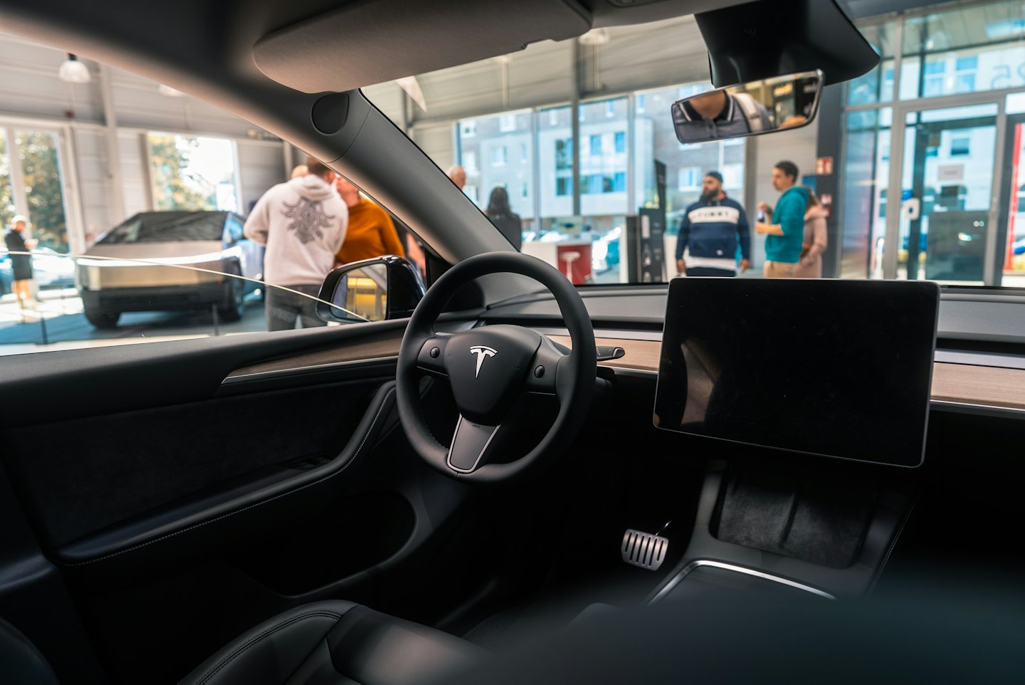 Modern electric car interior facing a busy car dealership showroom.