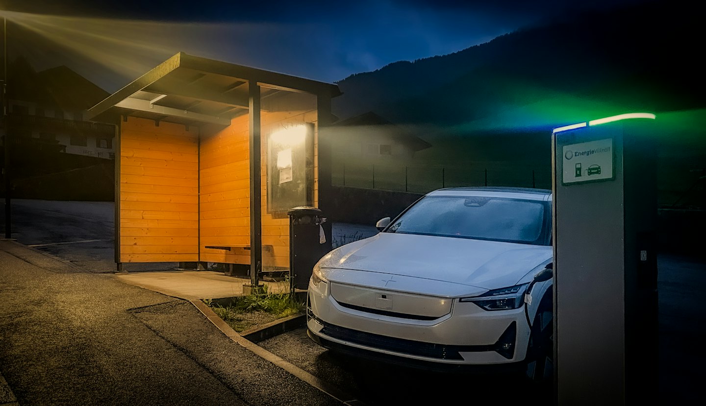 White electric vehicle charging at an outdoor station near a shelter.