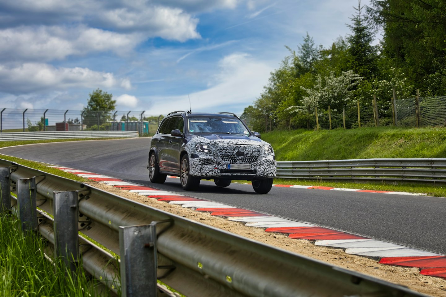 A camouflaged SUV drives around a curve on a racetrack.